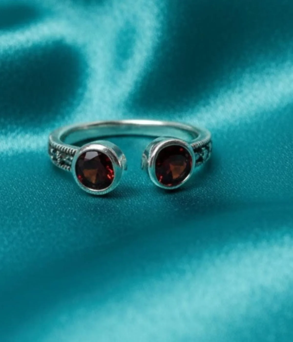 Sterling Silver Open Cuff Ring. Features a bypass design with two Bezel-set Red Garnet Style round stones at the ends. Adjustable and has a textured band.