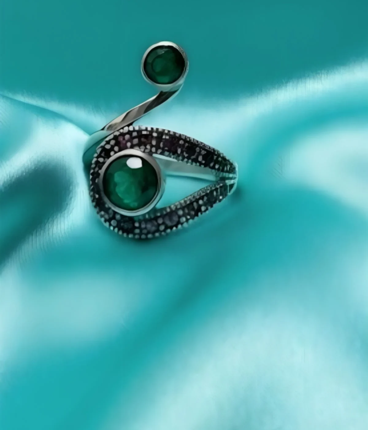 Sterling Silver Swirl Ring. Modern bypass design featuring two Green Emerald-style stones and contrasting Black Pave accents. Two-stone statement jewelry on a silk background.