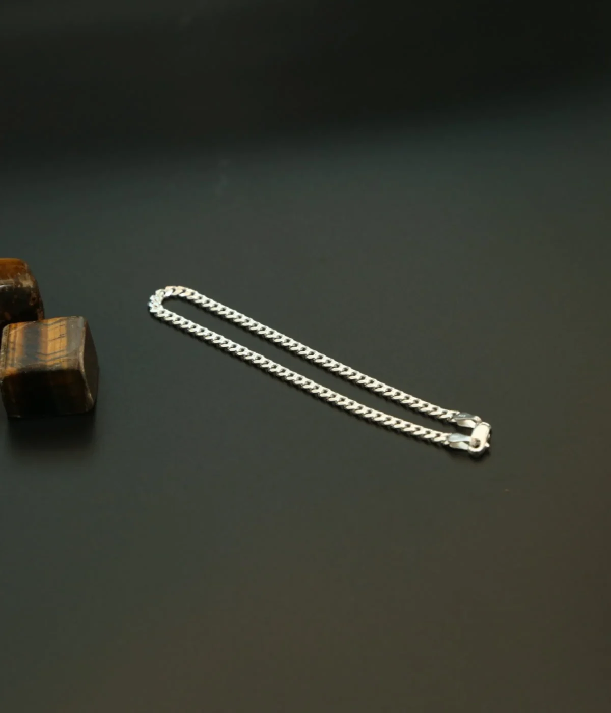 Men's Sterling Silver Curb Chain Bracelet (Cuban link style) displayed on a dark surface next to polished Tiger's Eye stones. A classic 925 Silver Link Kada.
