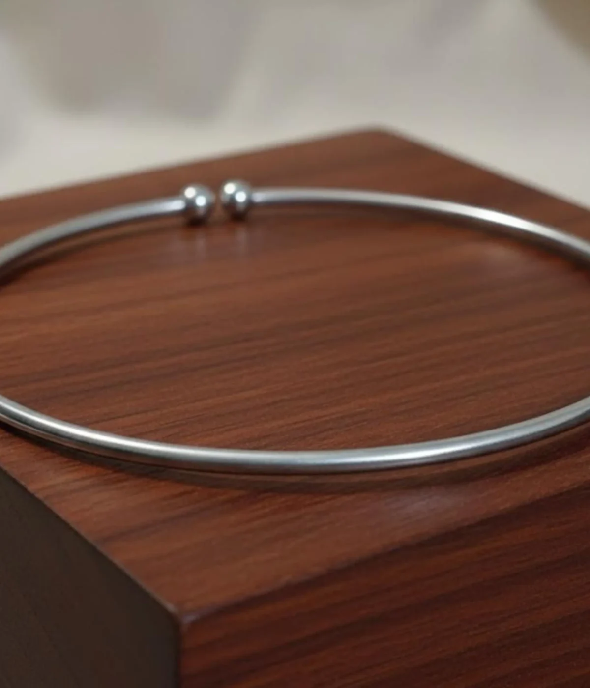 Minimalist Silver Rigid Collar Necklace. Sleek, thin open cuff choker with simple ball finials, displayed on a polished dark wooden block.