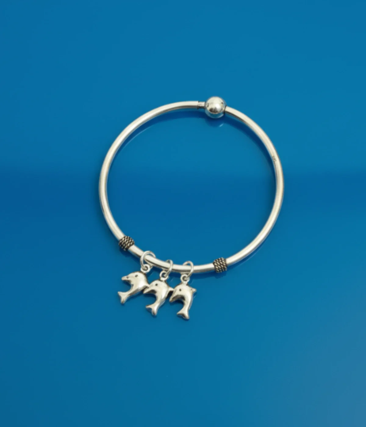 Silver charm bangle with three dolphin charms and small beaded accents. Ocean theme jewelry.