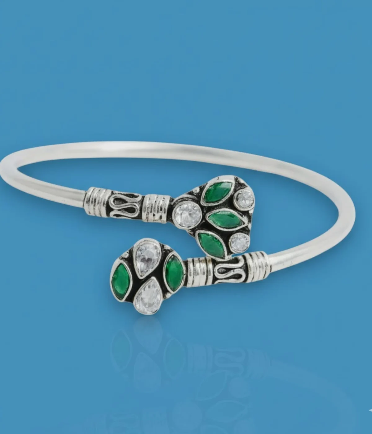 Sterling Silver Open Cuff Bangle. Features oxidized end pieces set with Emerald (green) and clear CZ cluster gemstones. Adjustable torque bracelet with a smooth silver band.