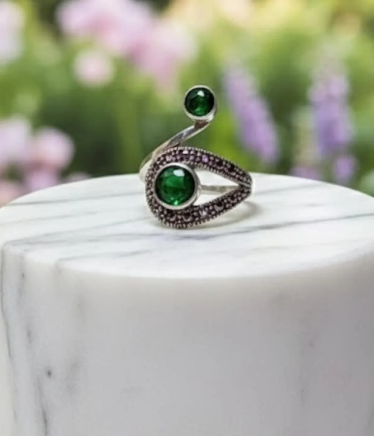 Sterling Silver Swirl Ring. Modern bypass design featuring two Green Emerald-style stones and contrasting Black Pave accents. Two-stone statement jewelry on a silk background.
