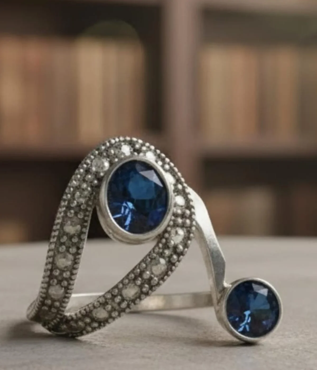 Vintage Style Blue Sapphire Bypass Ring. Sterling Silver two-stone design featuring a large oval and small round Sapphire Blue stone, accented with milgrain and clear pave details. Art Deco Statement Jewelry.