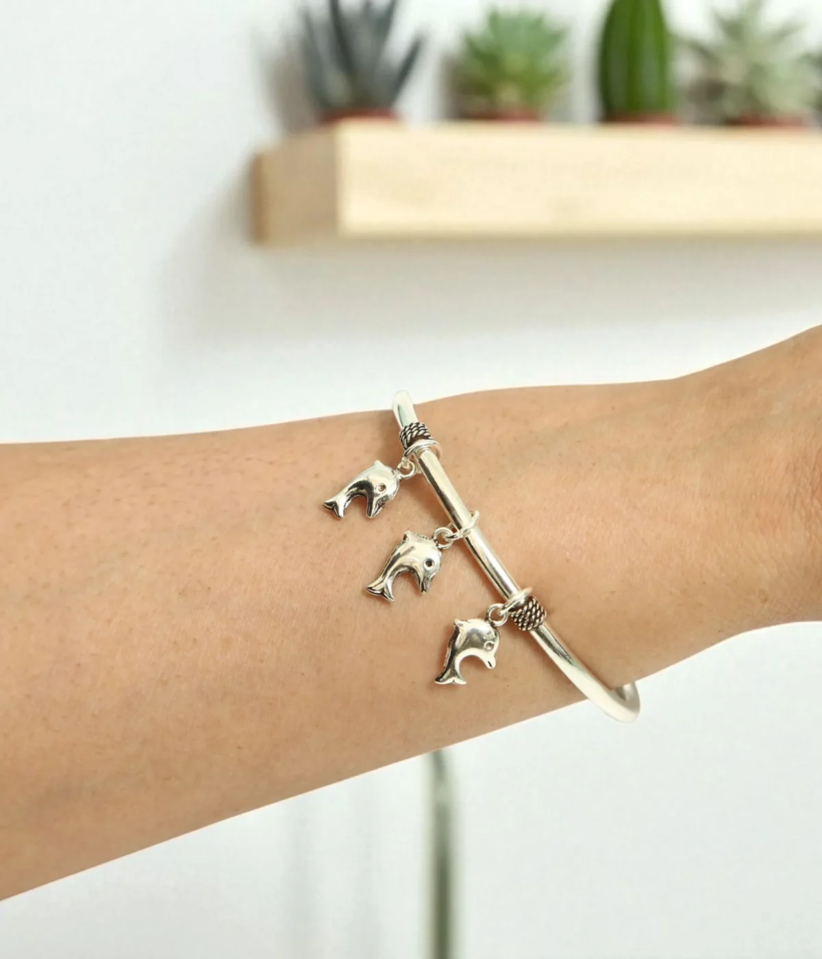 Silver charm bangle with three dolphin charms and small beaded accents. Ocean theme jewelry.