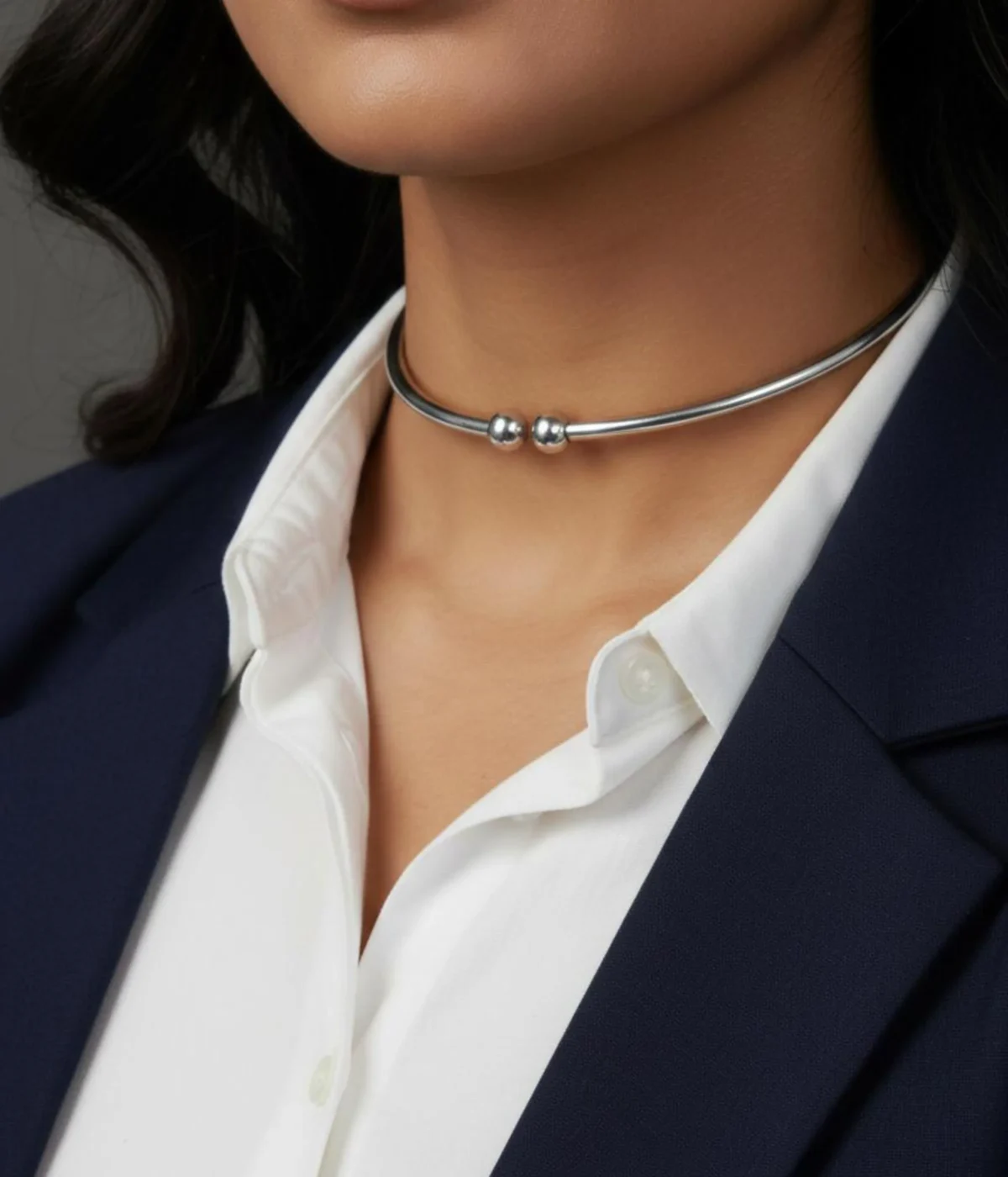 Minimalist Silver Rigid Collar Necklace. Sleek, thin open cuff choker with simple ball finials, displayed on a polished dark wooden block.