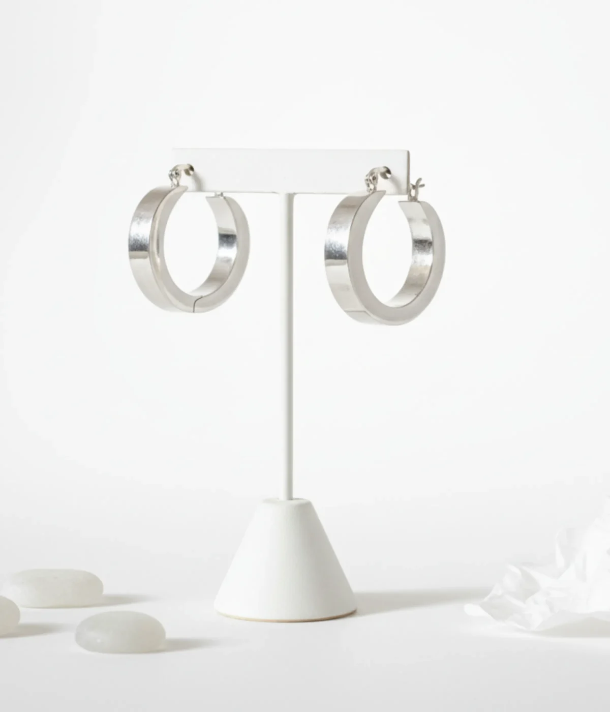 Pair of Chunky Silver Square Hoop Earrings. Thick, geometric hoops with a high polish finish, displayed on a white jewelry stand in a minimalist setting.