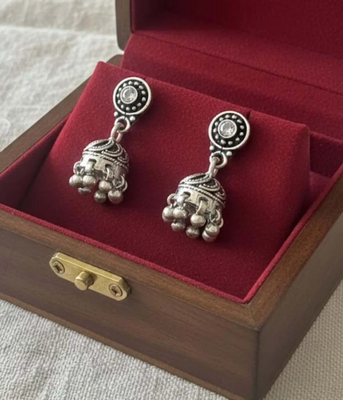 Pair of Oxidized Silver Jhumka Earrings. Traditional bell shape with crystal studs and ghungroo drops, displayed against a warm wooden background.