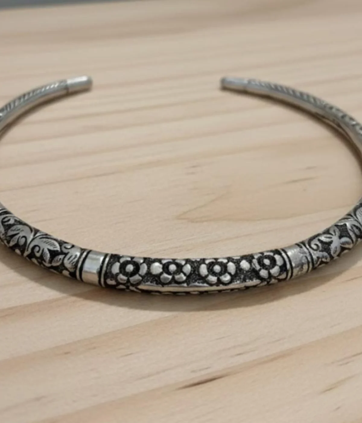 Oxidized Silver Floral Choker Necklace. Rigid, open cuff collar with detailed tribal engraving and an antique finish, displayed on ruffled teal silk fabric.