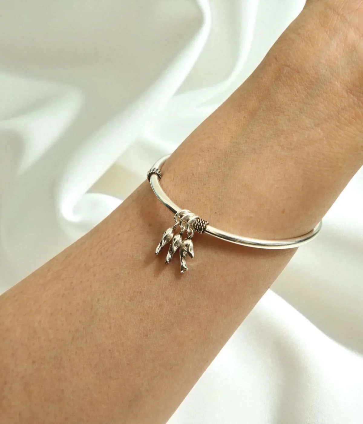 Silver charm bangle with three dolphin charms and small beaded accents. Ocean theme jewelry.