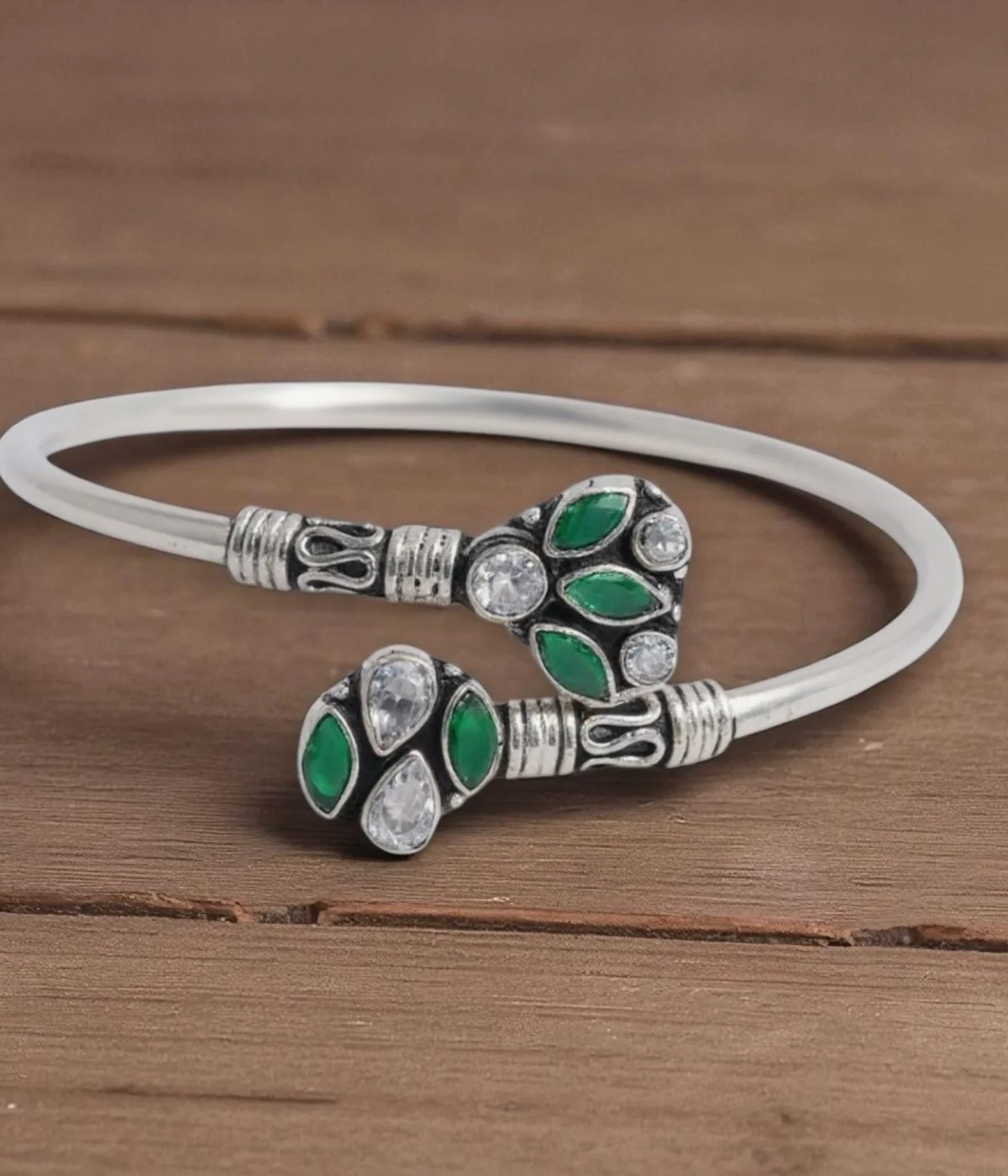 Sterling Silver Open Cuff Bangle. Features oxidized end pieces set with Emerald (green) and clear CZ cluster gemstones. Adjustable torque bracelet with a smooth silver band.