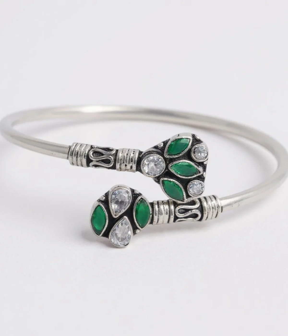 Sterling Silver Open Cuff Bangle. Features oxidized end pieces set with Emerald (green) and clear CZ cluster gemstones. Adjustable torque bracelet with a smooth silver band.