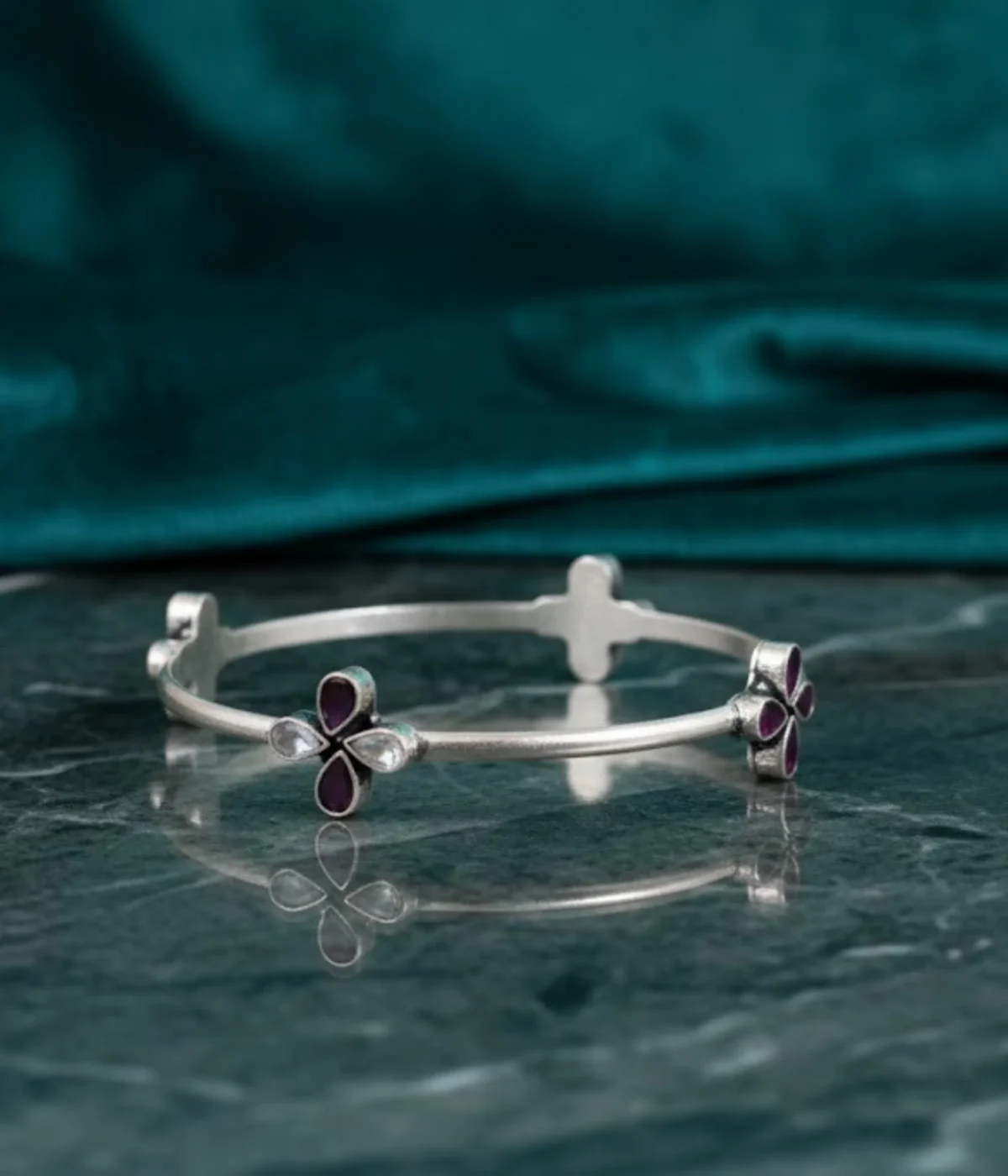 Sterling Silver Clover Bangle Bracelet. Features a fixed band and a central flower motif set with Magenta Ruby teardrop stones and White CZ accents. Minimalist Two-Tone Bangle.