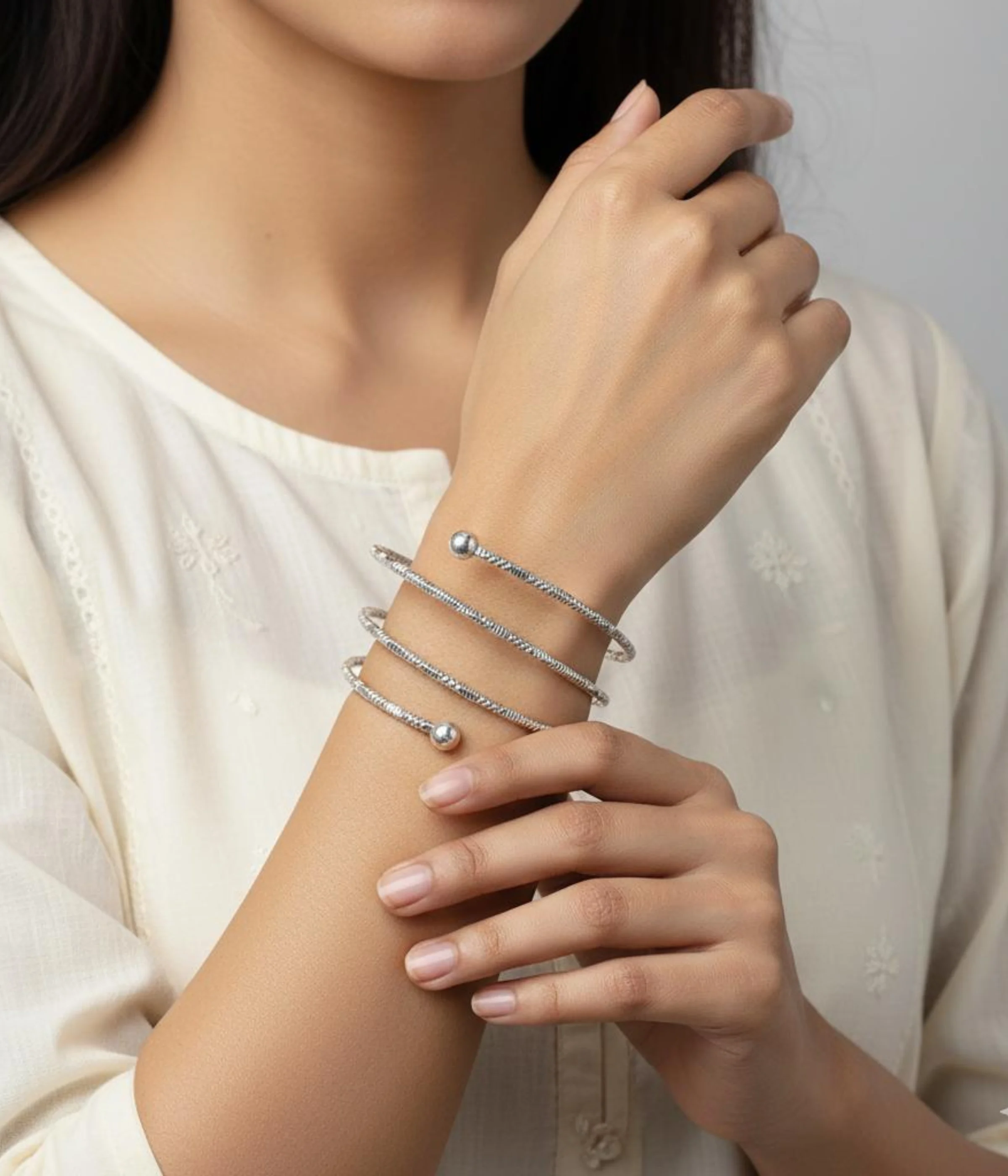 NeerSterling Silver Coiled Spiral Bracelet. Multi-turn textured silver wire wraps around itself with ball finials. Bohemian adjustable arm cuff on a blue satin background.