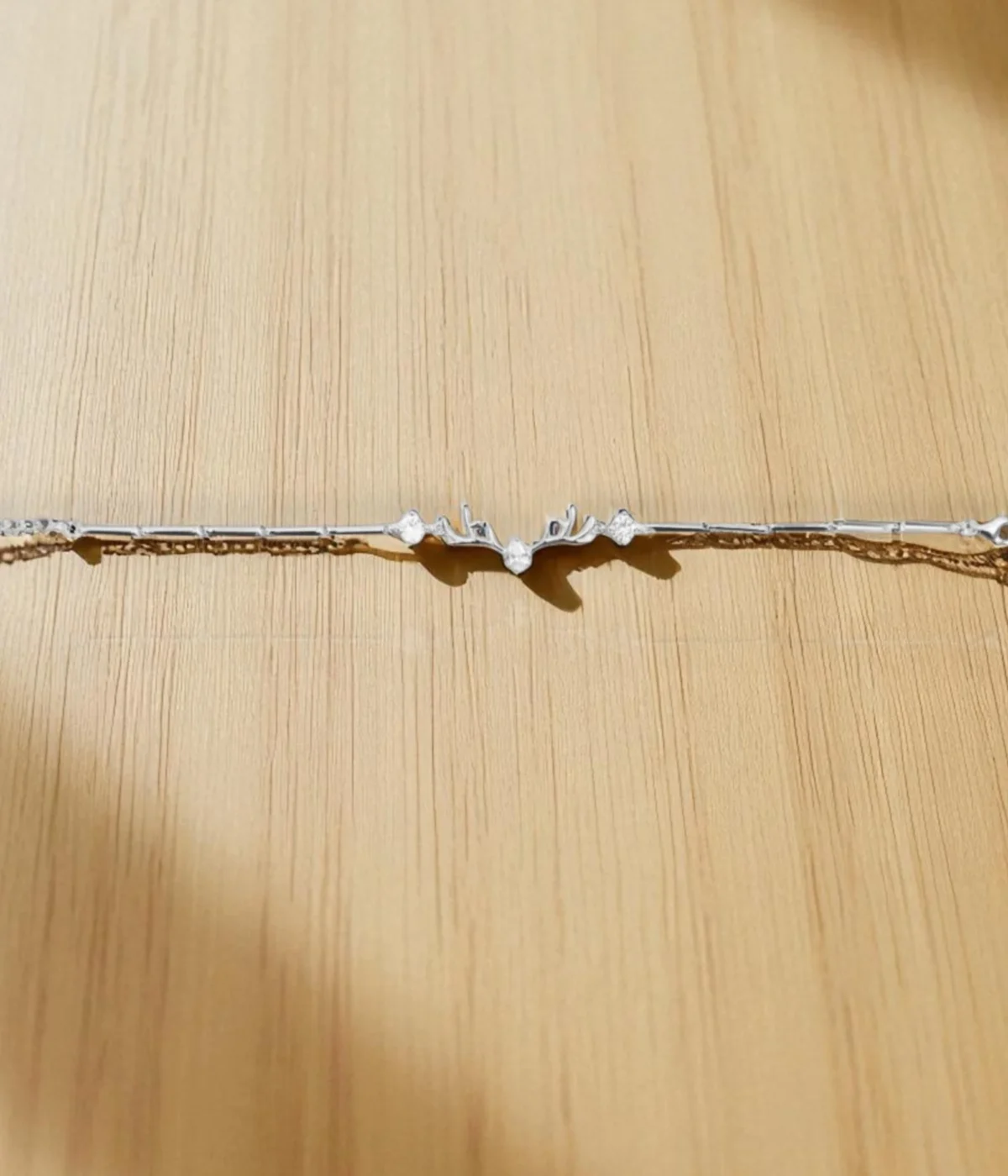 Sterling Silver Antler Charm Bracelet on a teal background. Features a minimalist reindeer antler motif accented with sparkling CZ stones. Dainty 925 silver nature-inspired jewelry for women.