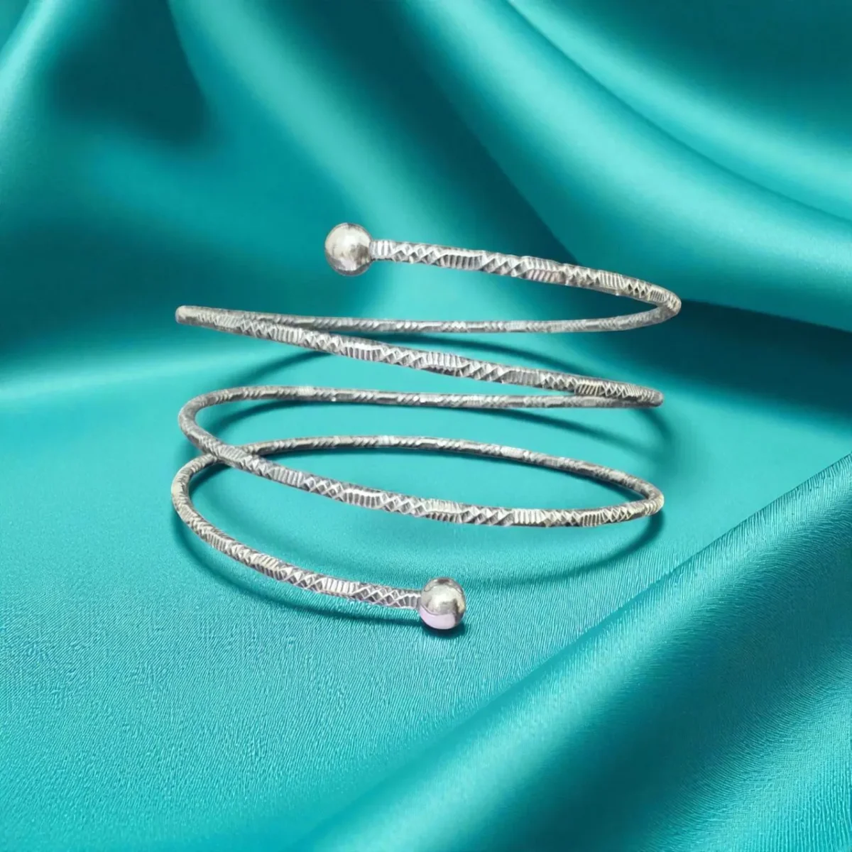 NeerSterling Silver Coiled Spiral Bracelet. Multi-turn textured silver wire wraps around itself with ball finials. Bohemian adjustable arm cuff on a blue satin background.