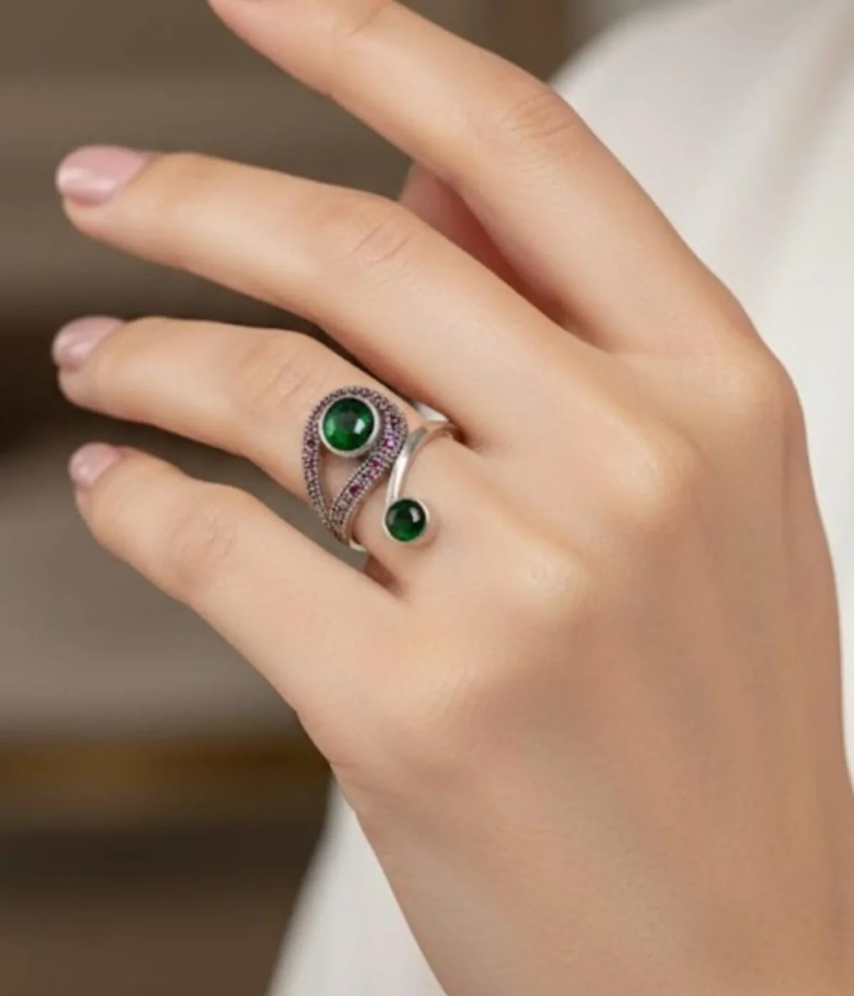 Sterling Silver Swirl Ring. Modern bypass design featuring two Green Emerald-style stones and contrasting Black Pave accents. Two-stone statement jewelry on a silk background.