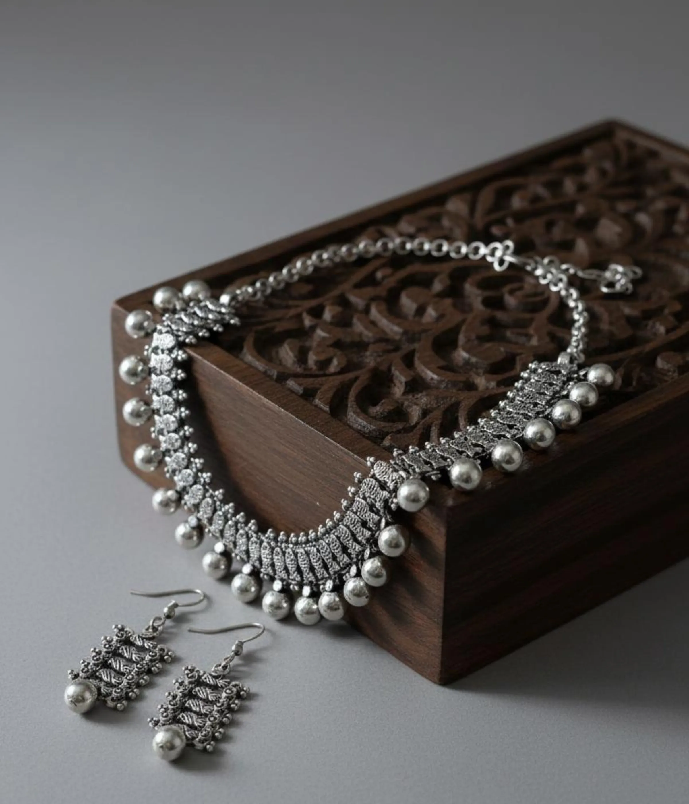 Oxidized Silver Ball Drop Necklace and Earring Set. Tribal choker with ball (Ghungroo) fringe and matching antique finish earrings, displayed on a carved wooden box.
