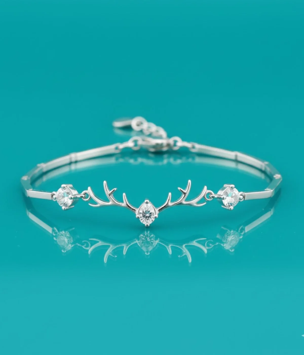 Sterling Silver Antler Charm Bracelet on a teal background. Features a minimalist reindeer antler motif accented with sparkling CZ stones. Dainty 925 silver nature-inspired jewelry for women.