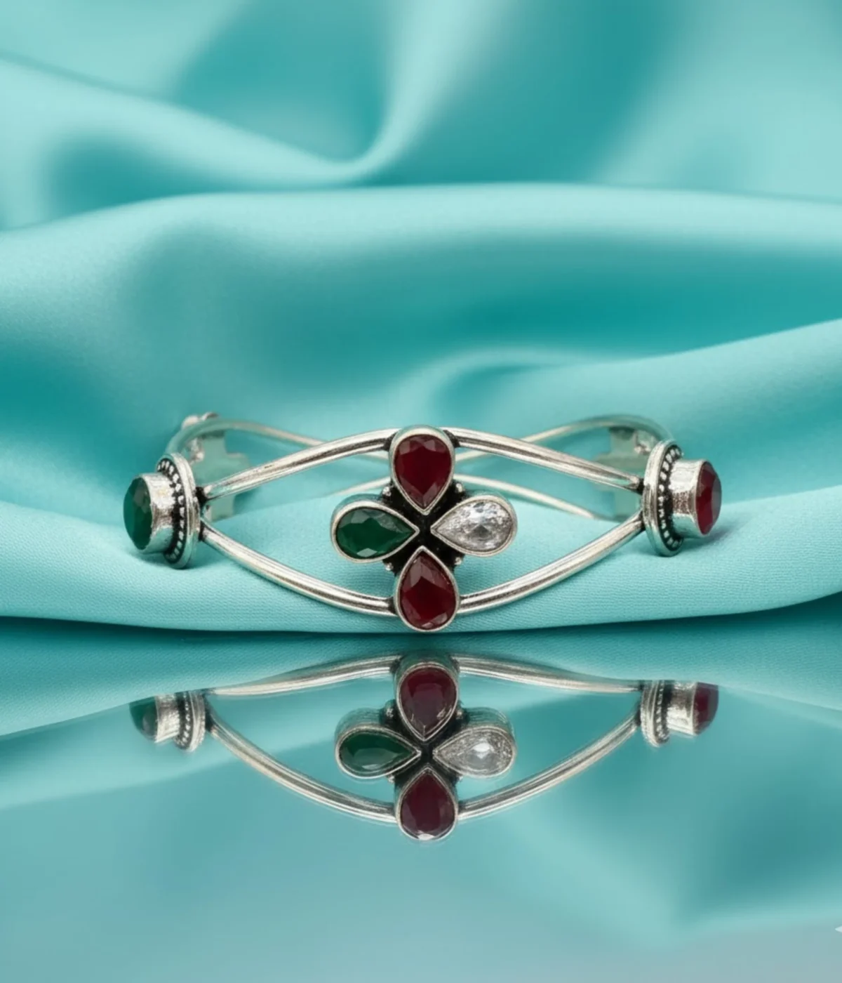 Neersterling Pair of Oxidized Sterling Silver Cuff Bangles worn on a woman's wrist. Ethnic Indian Kada style featuring prominent Ruby (red) and Emerald (green) gemstone accents on an antique finish.