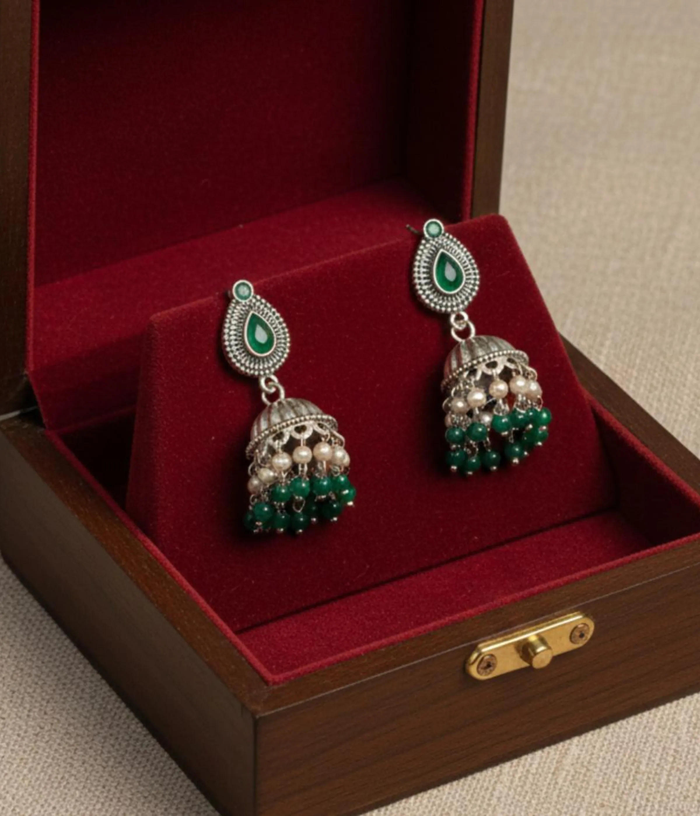 Traditional Oxidized Jhumka Earrings (12.5 gm) being worn. Features a Green Stone Stud, bell shape, and dangles made of small pearls and green beads. Indian Festive Ethnic Jewelry.