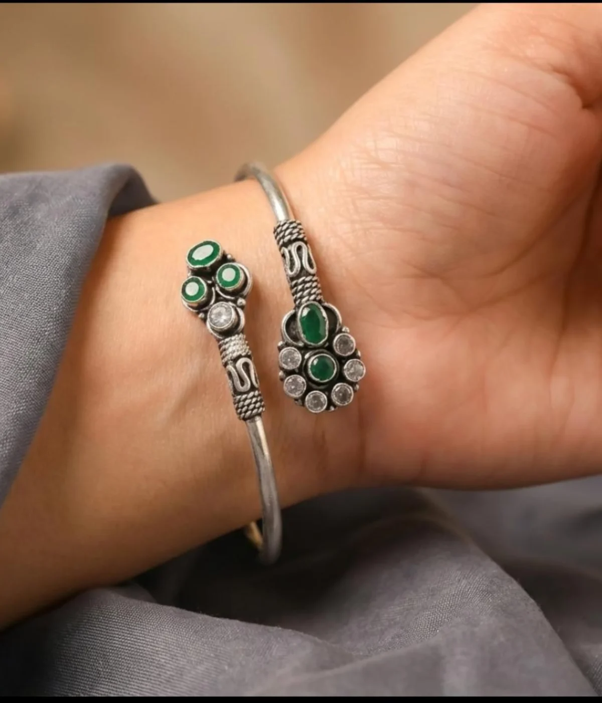 Detailed 17.1 gm oxidized silver floral kada featuring vibrant emerald green stones and clear zirconia accents on a white background.