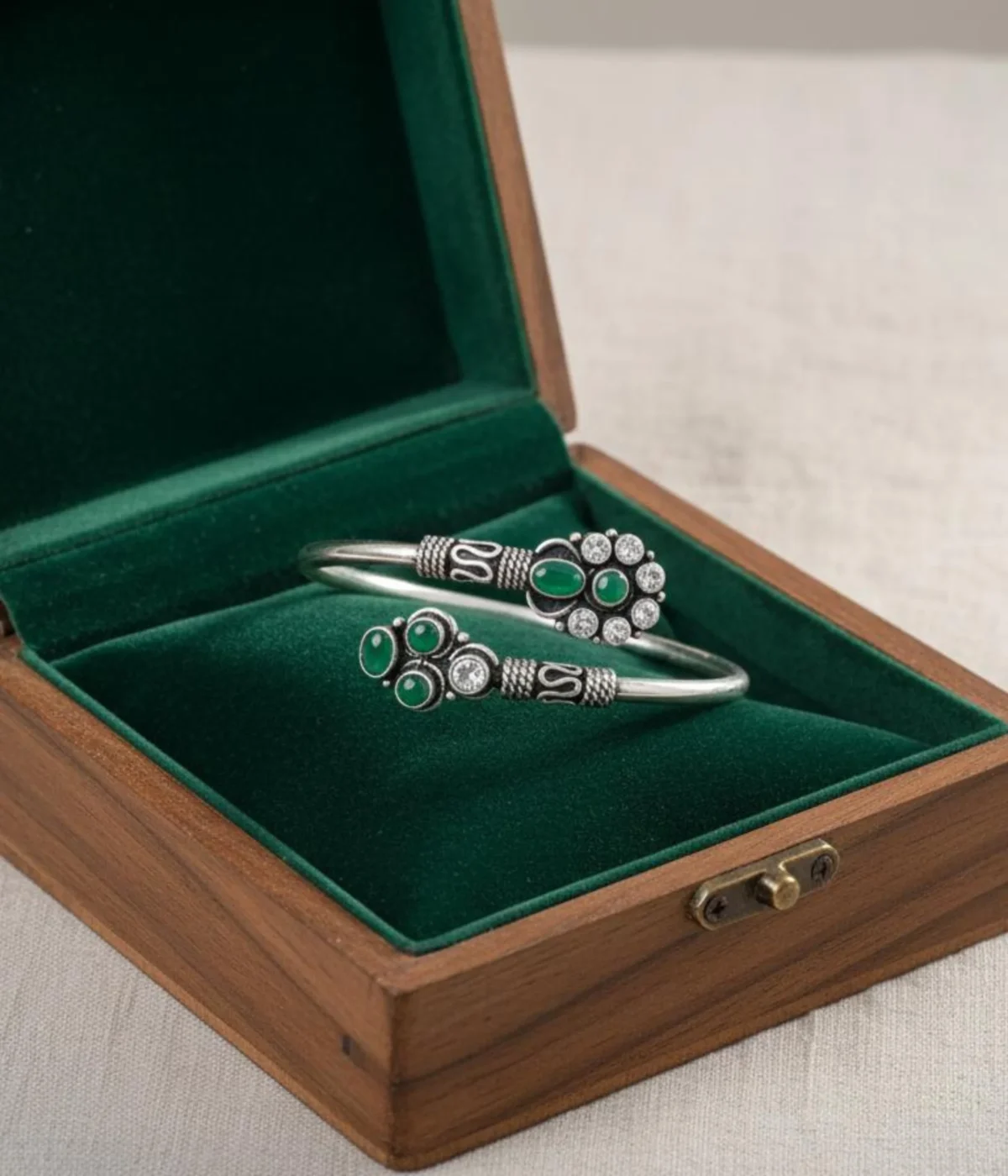 Detailed 17.1 gm oxidized silver floral kada featuring vibrant emerald green stones and clear zirconia accents on a white background.