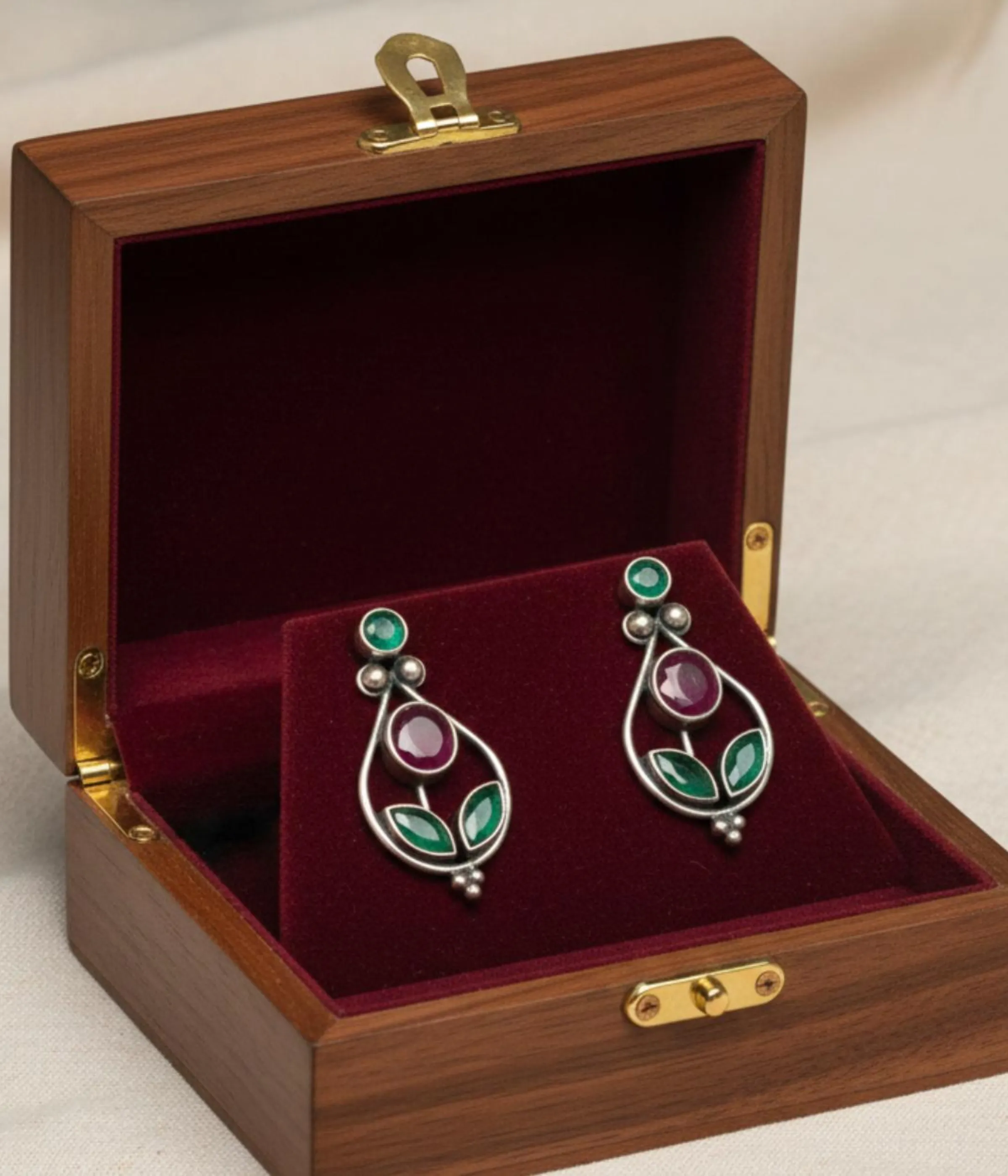 Pair of Oxidized Teardrop Dangle Earrings (5.9 gm). Ethnic style jewelry featuring Ruby and Green CZ Stones, displayed on a red velvet stand inside a dark wood gift box.
