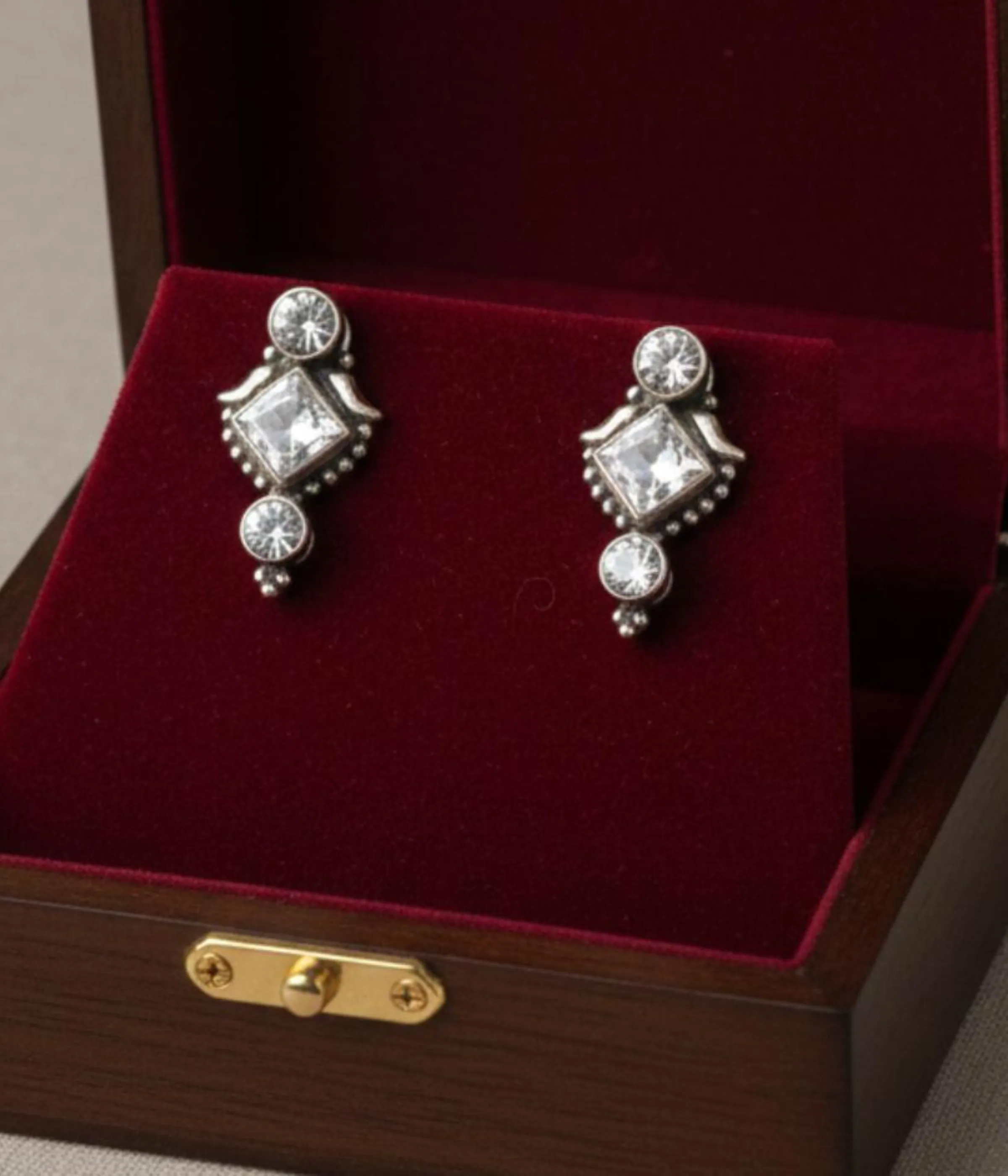 Pair of Oxidized Stud Drop Earrings. Vintage style silver tone dangles with a central Square CZ Stone, displayed in a velvet-lined wooden jewelry box.