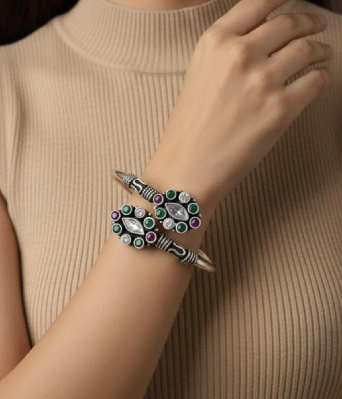 Detailed 16.3 gm oxidized silver floral kada featuring emerald green and maroon stones with clear zirconia accents on a wooden texture.