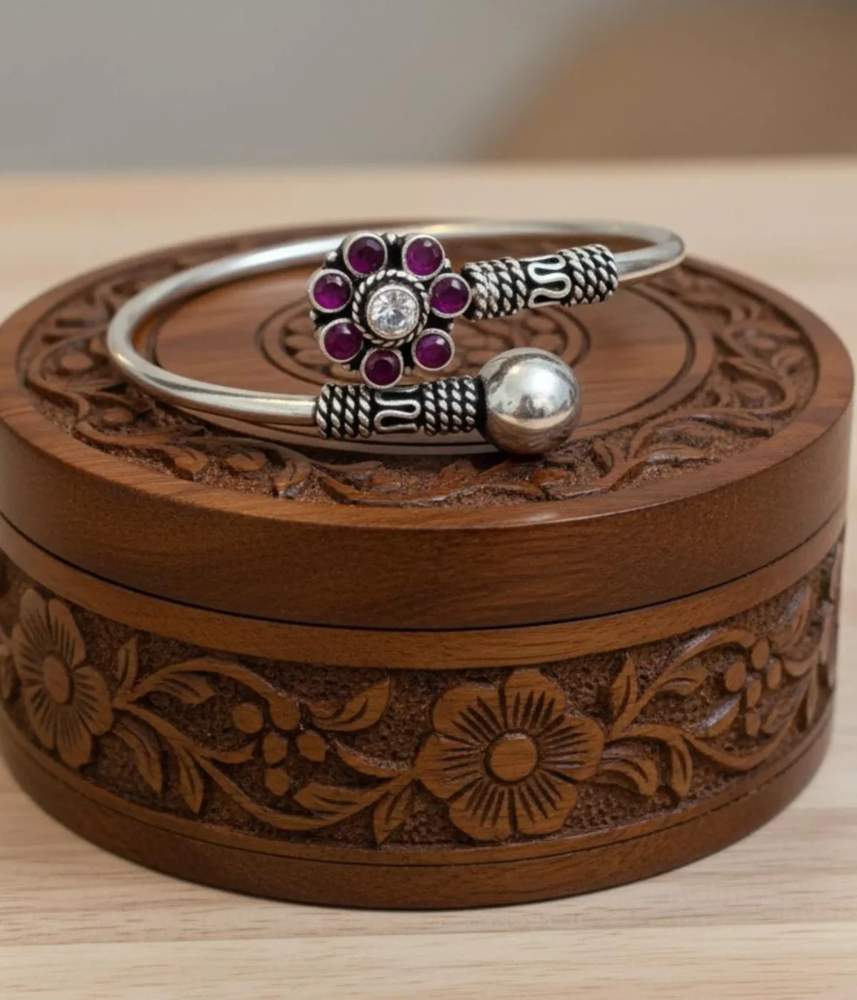 Handcrafted oxidized silver floral bangle featuring a ruby-pink gemstone flower centerpiece and an adjustable open-cuff design on a carved wooden box.