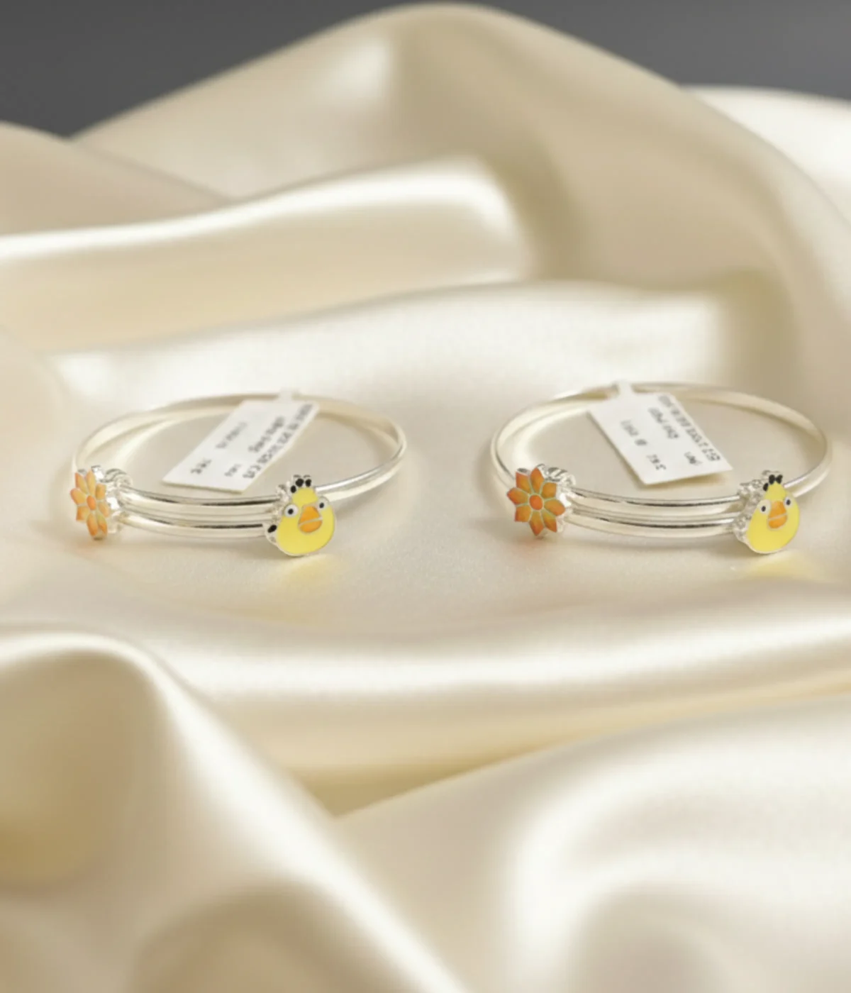 A 15.2g sterling silver kids bangle featuring twin daisy flower motifs at the ends with vibrant orange and yellow enamel work on a smooth adjustable band