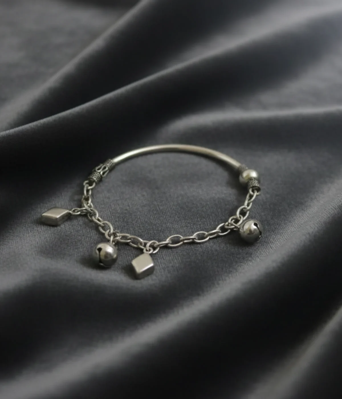Handcrafted 925 sterling silver kids bracelet weighing 12.5g with traditional bell charms on a dark grey silk background.