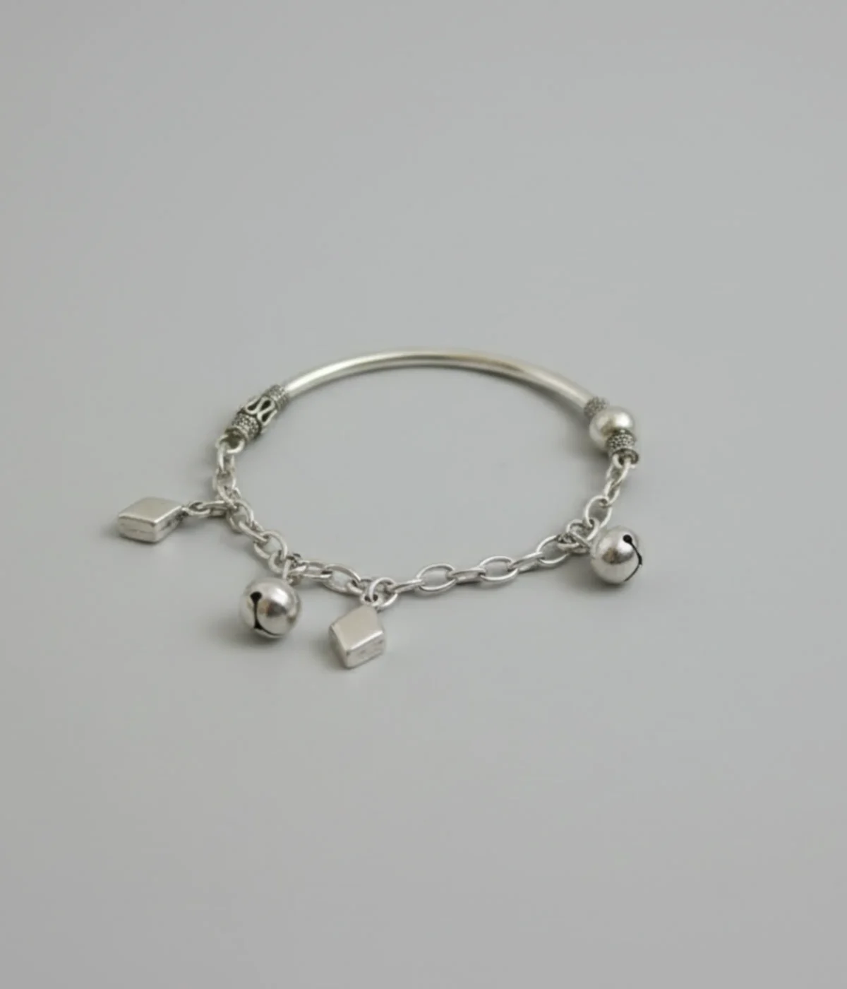 Handcrafted 925 sterling silver kids bracelet weighing 12.5g with traditional bell charms on a dark grey silk background.