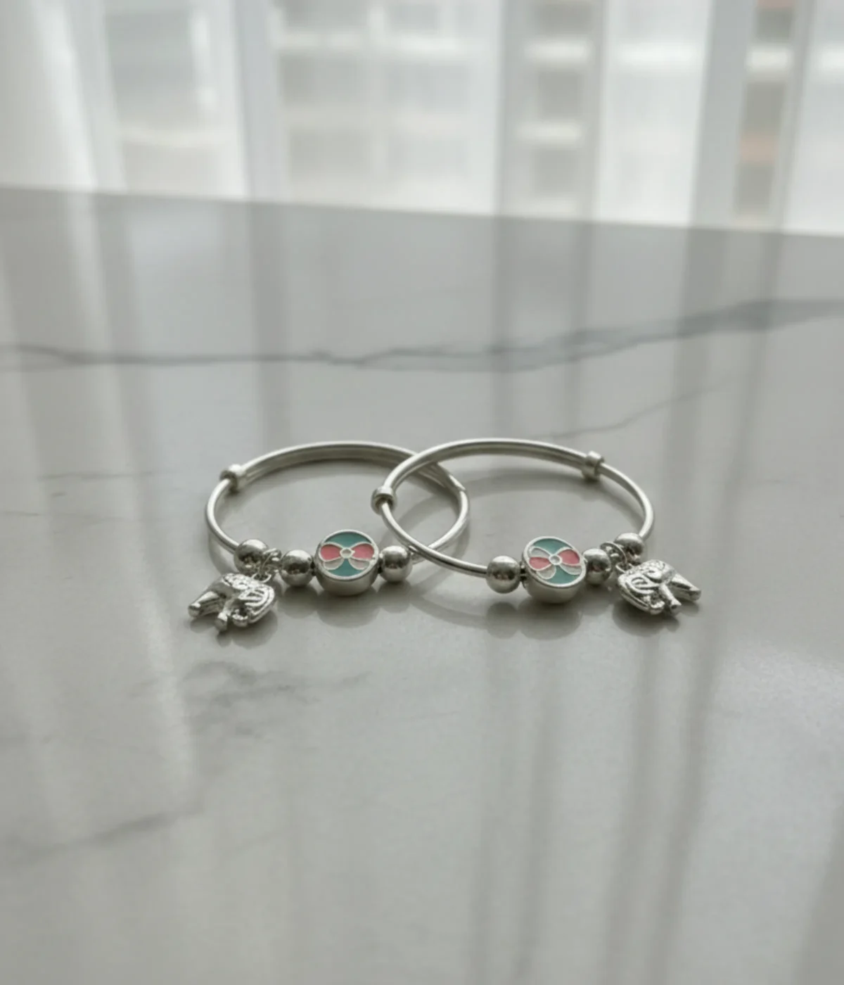 Handcrafted 925 sterling silver kids elephant bangle pair with pink and turquoise enamel charms shown on a child's wrist, 22.8g adjustable baby jewelry.
