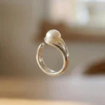 A minimalist silver plated adjustable ring featuring a sleek wrap-around band and a single, lustrous white pearl set in a modern open-style design.
