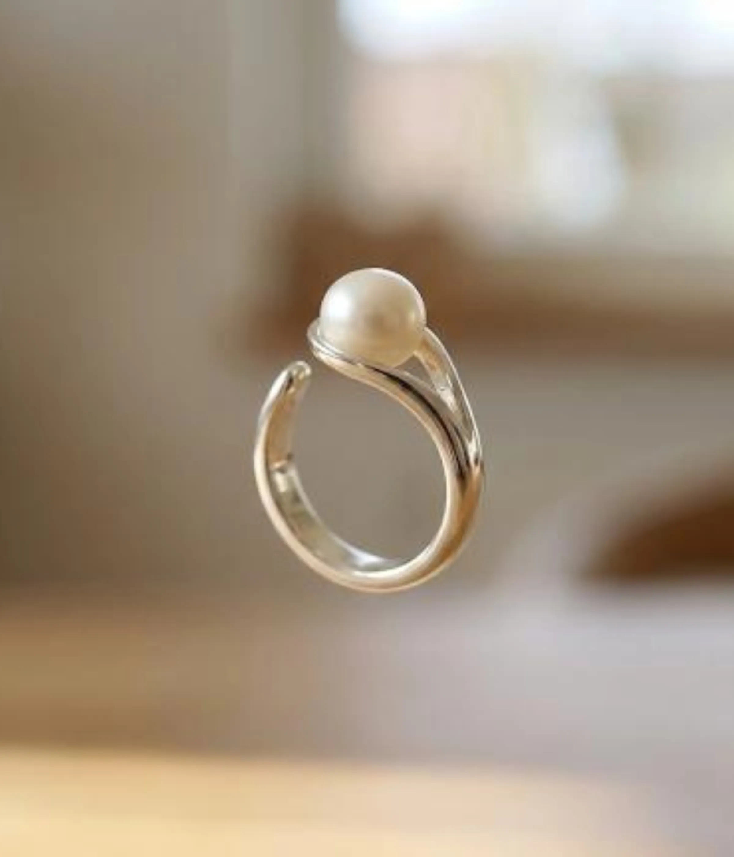 A minimalist silver plated adjustable ring featuring a sleek wrap-around band and a single, lustrous white pearl set in a modern open-style design.