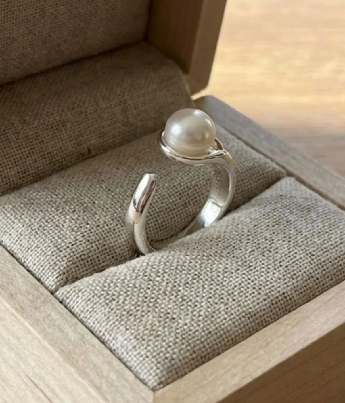 A minimalist silver plated adjustable ring featuring a sleek wrap-around band and a single, lustrous white pearl set in a modern open-style design.