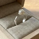 A minimalist silver plated adjustable ring featuring a sleek wrap-around band and a single, lustrous white pearl set in a modern open-style design.