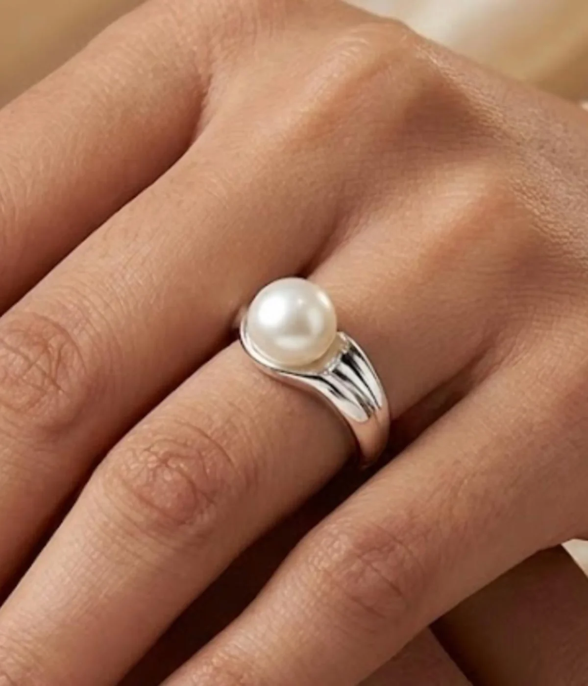 A minimalist silver plated adjustable ring featuring a sleek wrap-around band and a single, lustrous white pearl set in a modern open-style design.