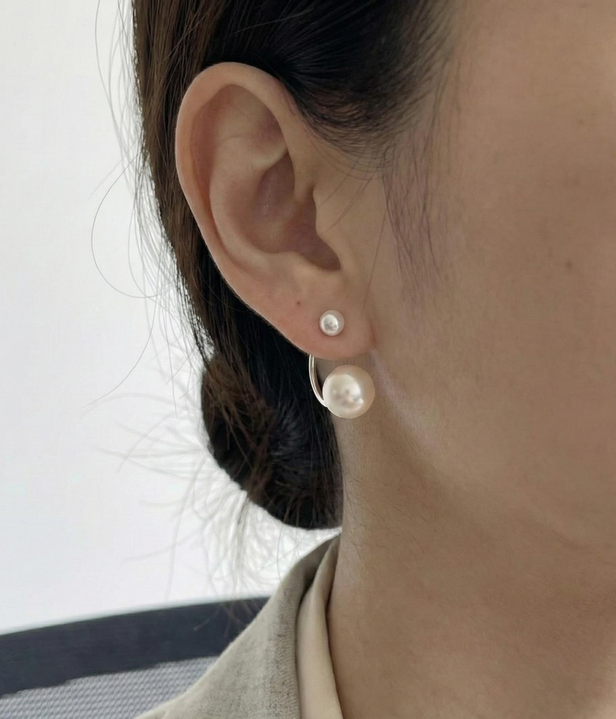 A pair of silver-plated front-back earrings featuring a minimalist "jacket" design with a small white pearl on the front stud and a larger white pearl that curves from behind the earlobe.