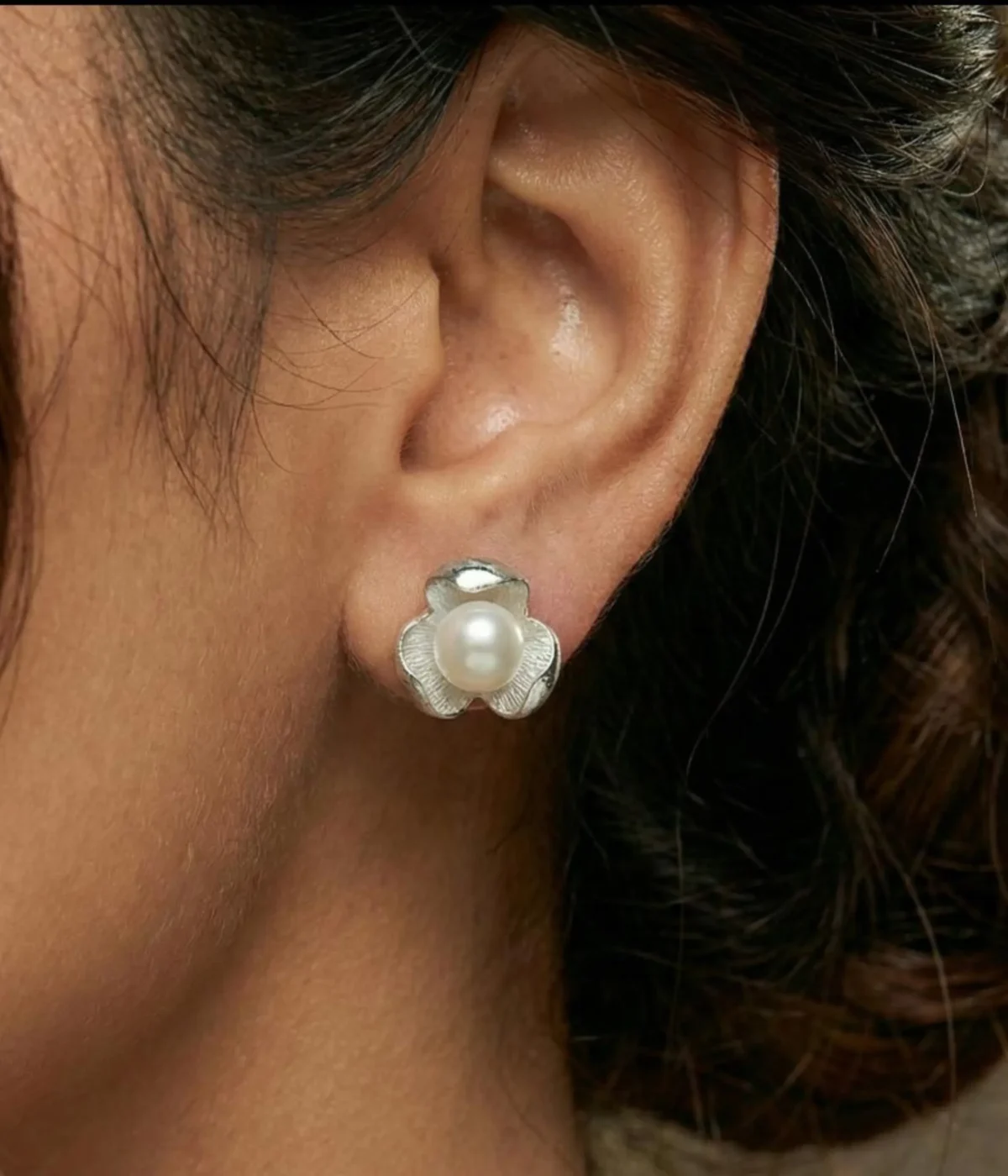 A pair of silver-plated stud earrings featuring a lustrous white pearl centered within a three-petal lotus blossom design, finished with a contemporary brushed matte texture.