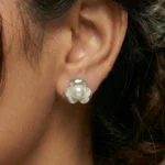 A pair of silver-plated stud earrings featuring a lustrous white pearl centered within a three-petal lotus blossom design, finished with a contemporary brushed matte texture.