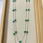 A long 925 sterling silver station necklace featuring vibrant green round gemstones set in polished silver bezel frames, elegantly displayed on a neutral fabric background within a wooden jewelry tray.