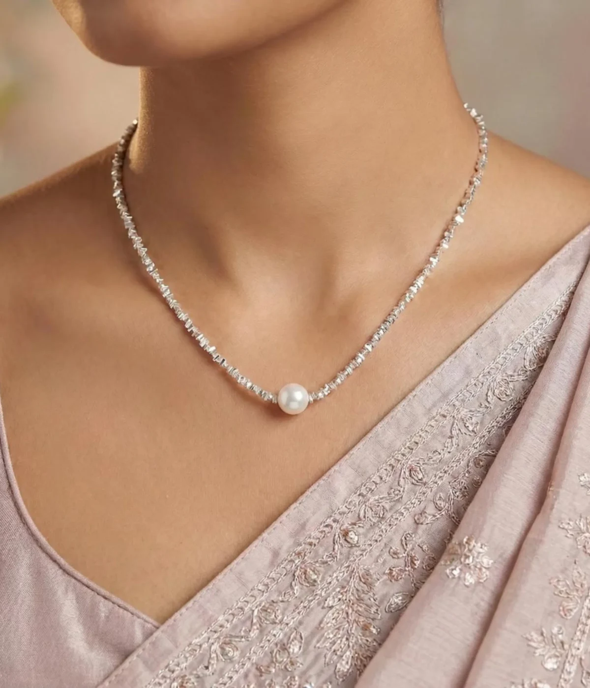 A delicate silver-plated necklace with a shimmering, textured chain and a single, central white pearl, displayed inside a wooden jewelry box on a soft cream-colored cushion.