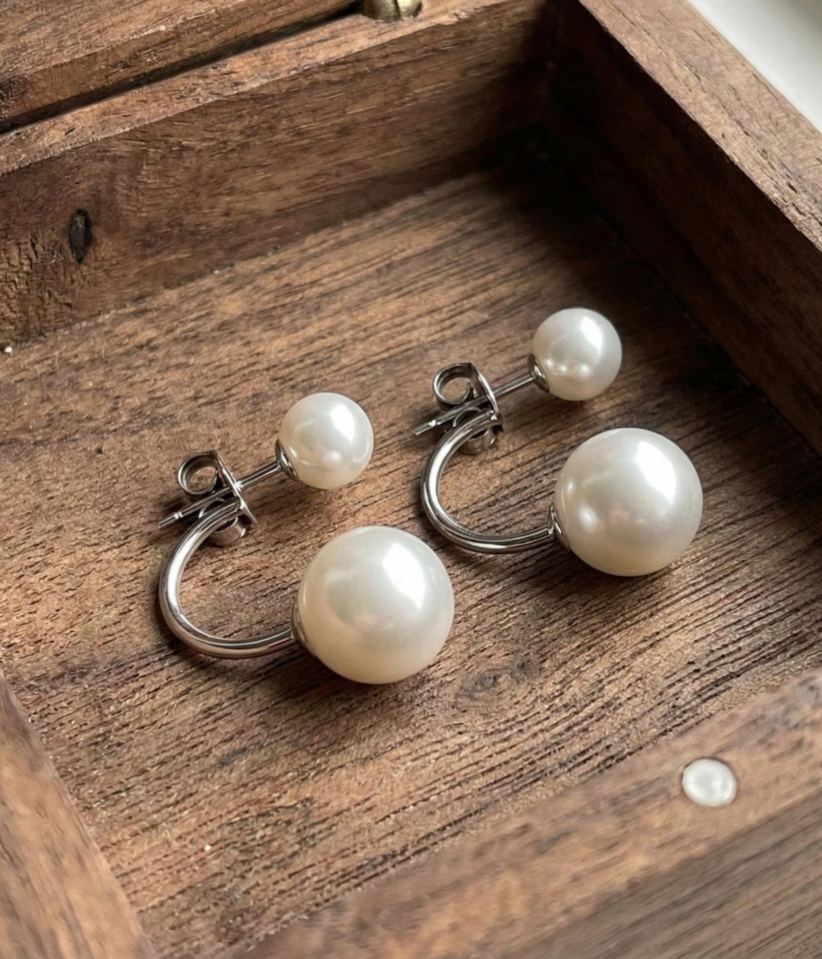 A pair of silver-plated front-back earrings featuring a minimalist "jacket" design with a small white pearl on the front stud and a larger white pearl that curves from behind the earlobe.