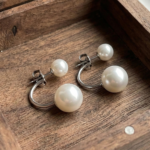 A pair of silver-plated front-back earrings featuring a minimalist "jacket" design with a small white pearl on the front stud and a larger white pearl that curves from behind the earlobe.