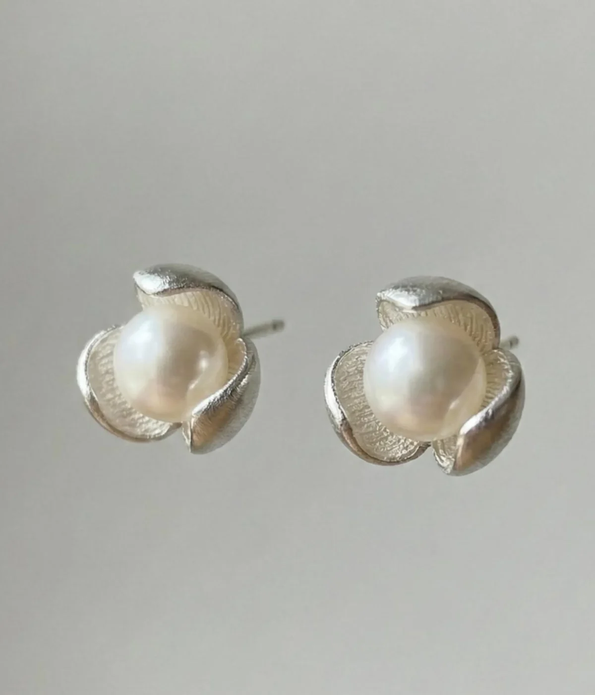 A pair of silver-plated stud earrings featuring a lustrous white pearl centered within a three-petal lotus blossom design, finished with a contemporary brushed matte texture.