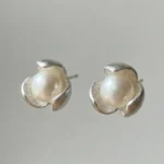 A pair of silver-plated stud earrings featuring a lustrous white pearl centered within a three-petal lotus blossom design, finished with a contemporary brushed matte texture.