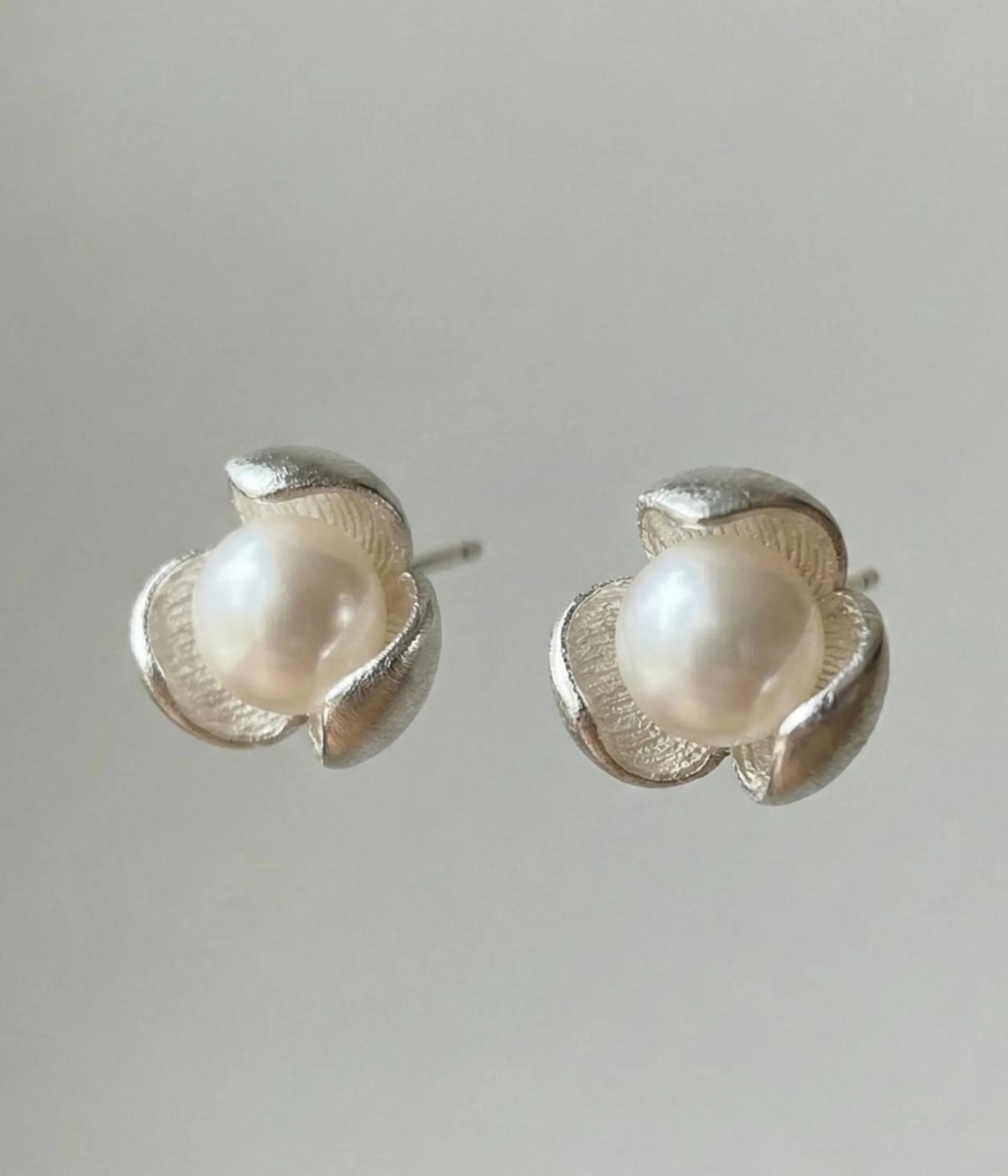 A pair of silver-plated stud earrings featuring a lustrous white pearl centered within a three-petal lotus blossom design, finished with a contemporary brushed matte texture.